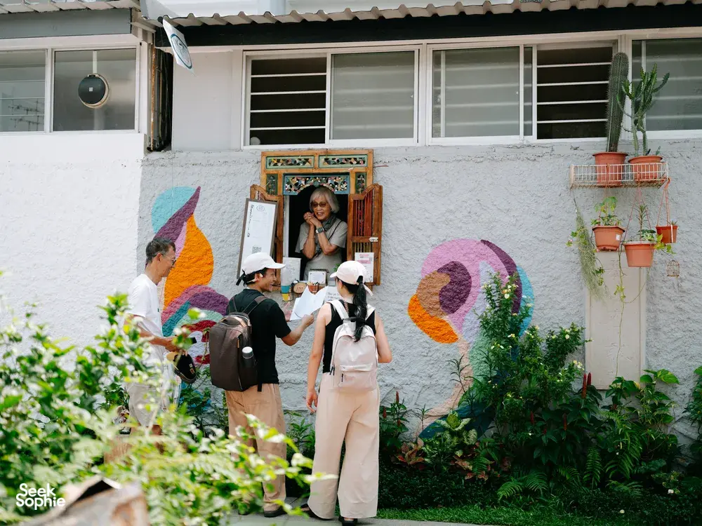 People on a Joo Chiat photo walk gather by a colourful courtyard mural, talking and holding cameras in Singapore