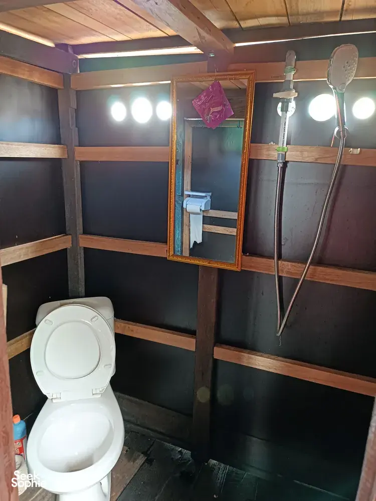 Boat bathroom on board with a white toilet, wall lights, and a mirror inside wooden bunk walls on a 3D2N cruise, Tanjung Puting