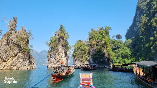 Multiple long-tail boats moored along steep cliffs while travellers prepare to continue the journey at Cheow Lan Lake