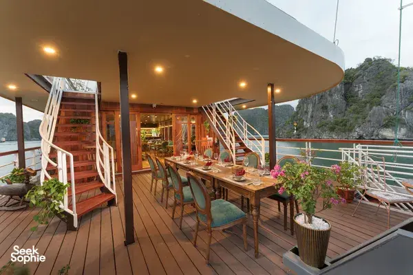 Alfresco dining deck on Cat Ba Ocean Cruises, with set tables and chairs overlooking Lan Ha Bay and limestone cliffs