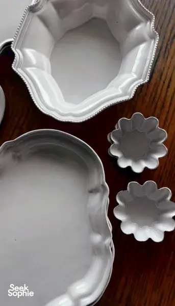 Close-up of embossed white ceramic plates with scalloped rims resting on a wooden surface, showing antique-inspired detailing