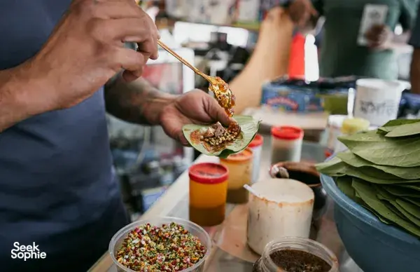 Tangan menyajikan hidangan pembuka ke piring beralas daun di atas meja, dari Hidden Heritage dalam pengalaman hidden gems Secrets of the Streets di Singapura