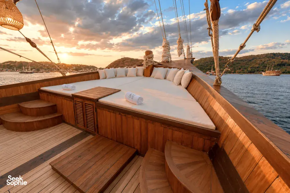 Sunset on a phinisi deck with cushioned lounge benches, railing steps and harbour views across the water in Labuan Bajo