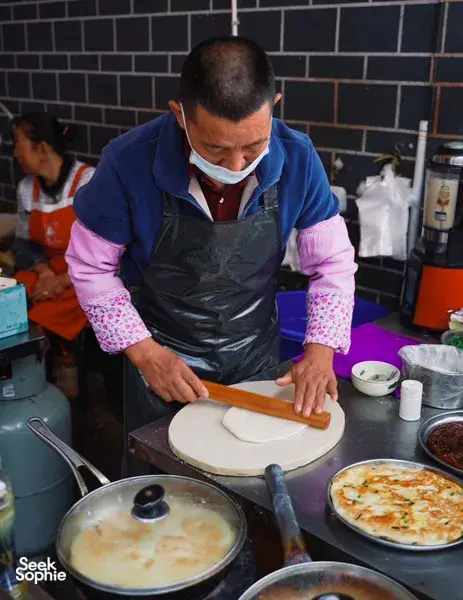 Cook preparing dough for flatbread on a wooden board in a backstreet kitchen during a Lijiang food hunt