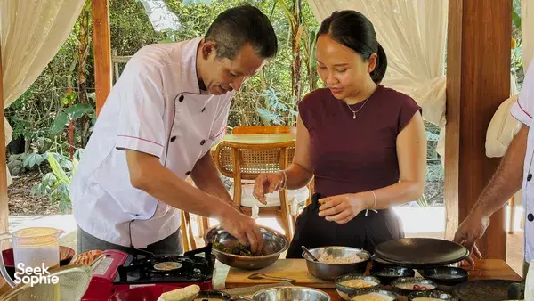 Chef and participant sautéing plant-based vegetables at a Manggarai vegan cooking class with skillets on the stove in Labuan Bajo
