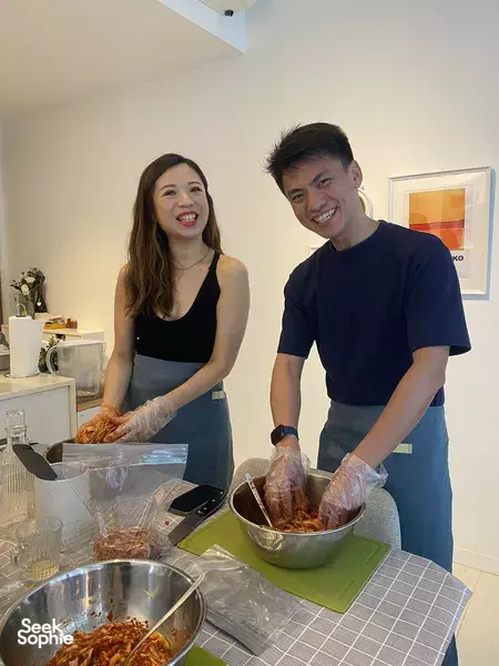 Gloved participants preparing fresh kimchi at a kitchen table, smiling while handling ingredients during Korean workshops in Singapore