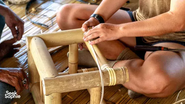Close-up of hands binding a bamboo joint with cord on a woodworking table during a class in Indonesia
