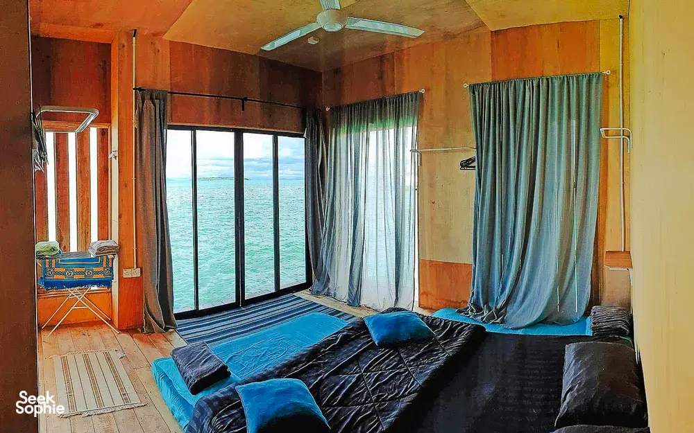 Sea lodge bedroom in Semporna with a double bed, blue curtains and floor-to-ceiling windows looking out to the ocean