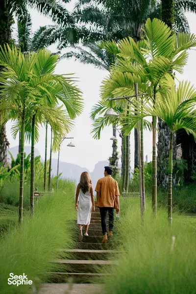 Couple strolling along a garden path lined with tall palm trees during a camping stay in Thailand