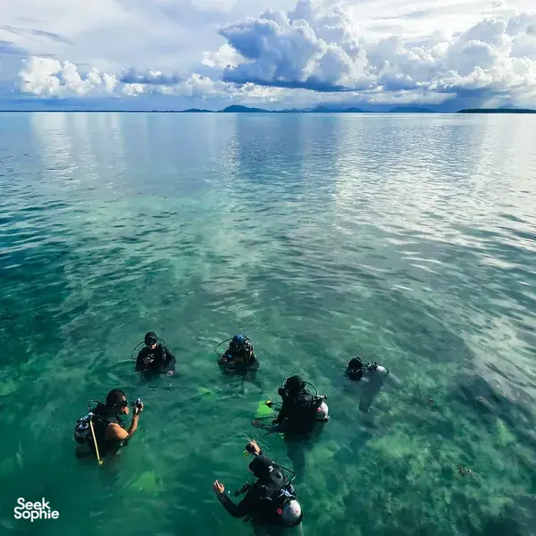 Scuba divers equipped with fins and tanks floating over clear shallow reef water off Semporna for a 2D1N dive & stay