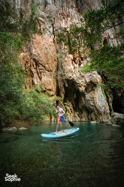 Stand-up paddler gliding through calm green water beneath limestone cliffs at Phong Nha on the 2D1N trek