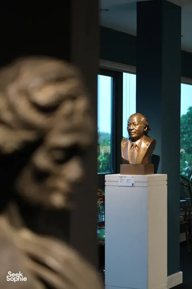 Bronze bust sculpture on a pedestal inside Quang San Art Museum, with a blurred stone artwork in the foreground, Ho Chi Minh City