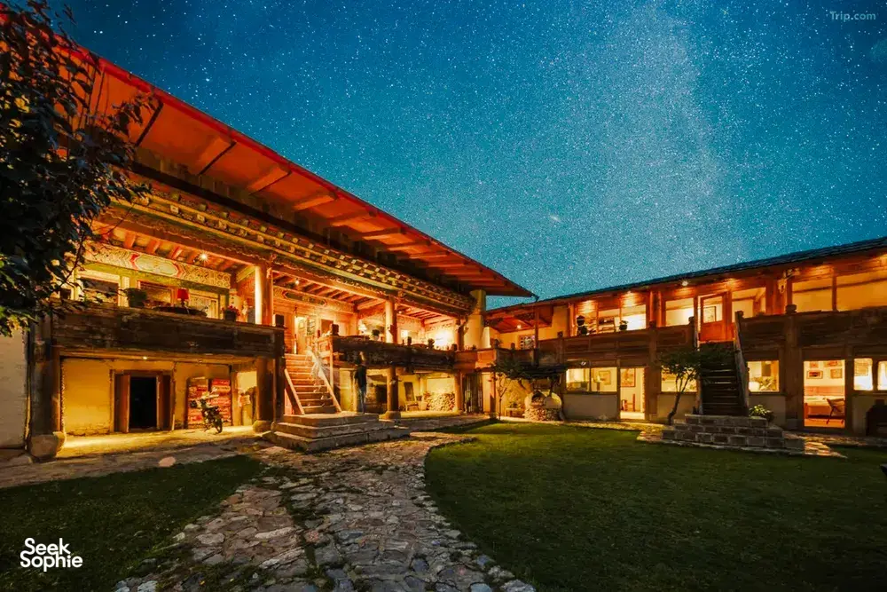Starlit courtyard at Ferme Liotard in Shangri-La, with warm wooden verandas and a stone path for a Tibetan mountain valley stay