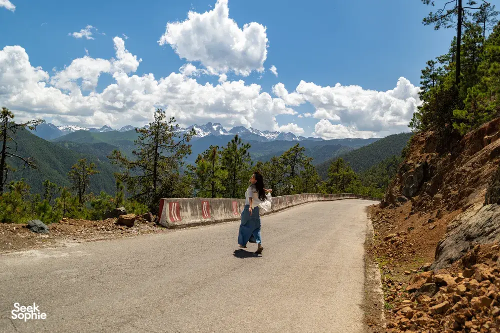 Walker on a mountain road near Shangri-La, with Meili Snow Mountain’s snowy peaks across the valley under blue sky
