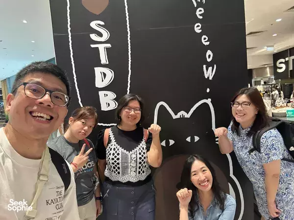 Smiling team posing by a cat-themed wall inside a café while playing a host-led Chinatown game in Singapore hidden gems