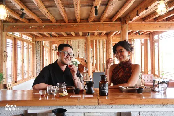 Rustic Lijiang coffee tasting at a family workshop, two guests smiling as they sip from cups beside pour-over brewers