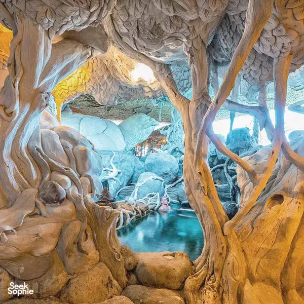 Mineral spa grotto with carved wooden roots surrounding a bright blue pool, indoors for relaxation at the retreat, Canggu