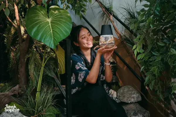 Smiling guest holding a miniature moss lamp with a landscape in The Mossiah’s Singapore biophilic studio during workshops in Singapore
