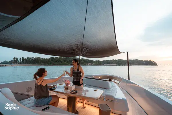 Two guests relaxing on Mare Mio Italian luxury yacht in Singapore at sunset, dining under the canopy on a calm evening cruise