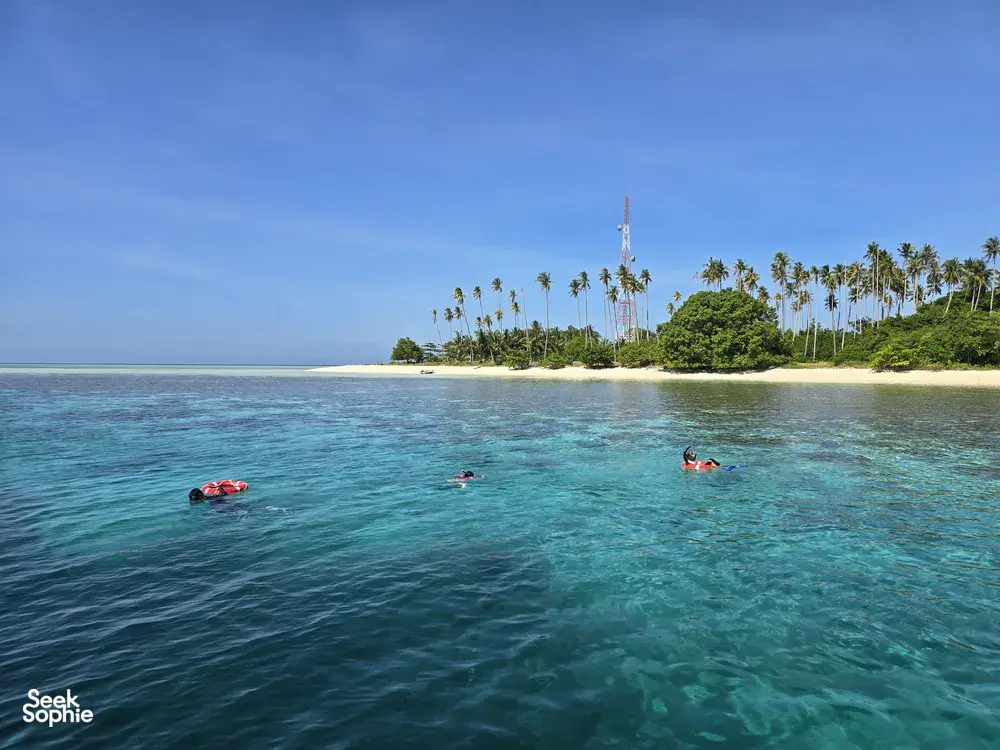 Sehari snorkeling di kepulauan Semporna: kayak merah berhampiran beting pasir berbaris pokok palma di atas air biru firus yang jernih, bersama Bigfin Divers