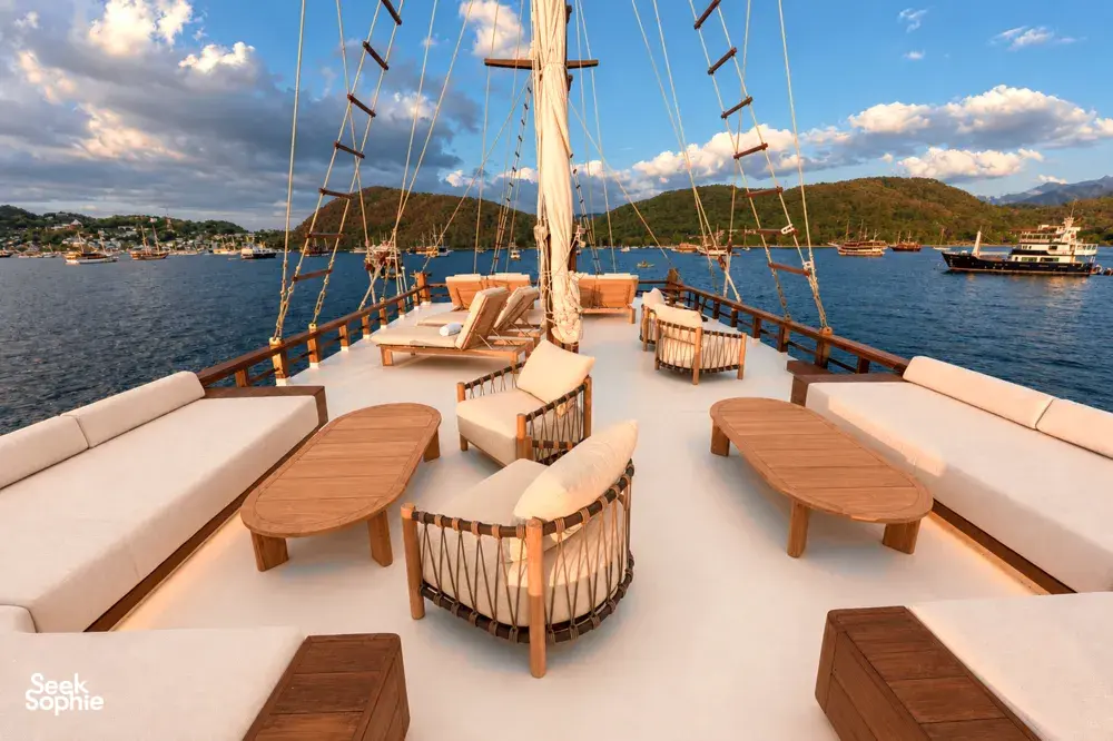 Komodo Island phinisi sundeck with beige daybeds and wooden tables, sail rig overhead on a Travass Life shared cruise
