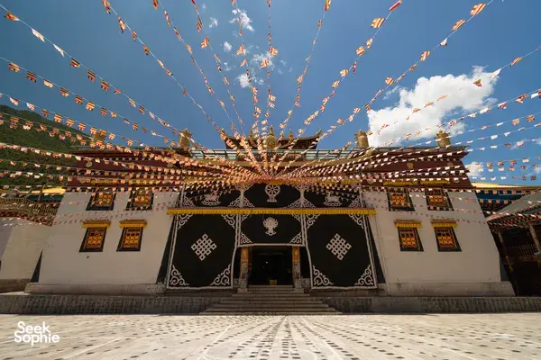 Tibetan prayer flags strung above a monastery courtyard in Shangri-La, with ornate walls under blue sky