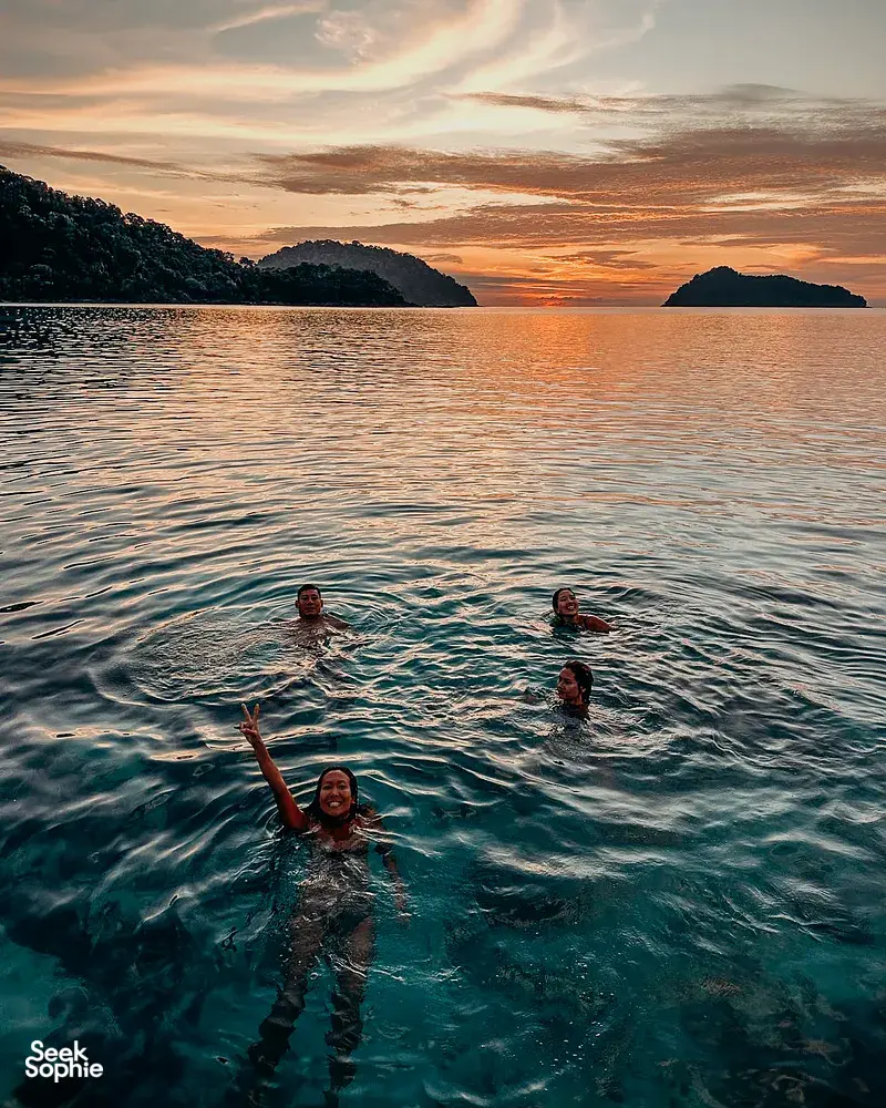 People floating and swimming at sunset in calm Andaman Sea water during Surin Island beach camping and snorkelling