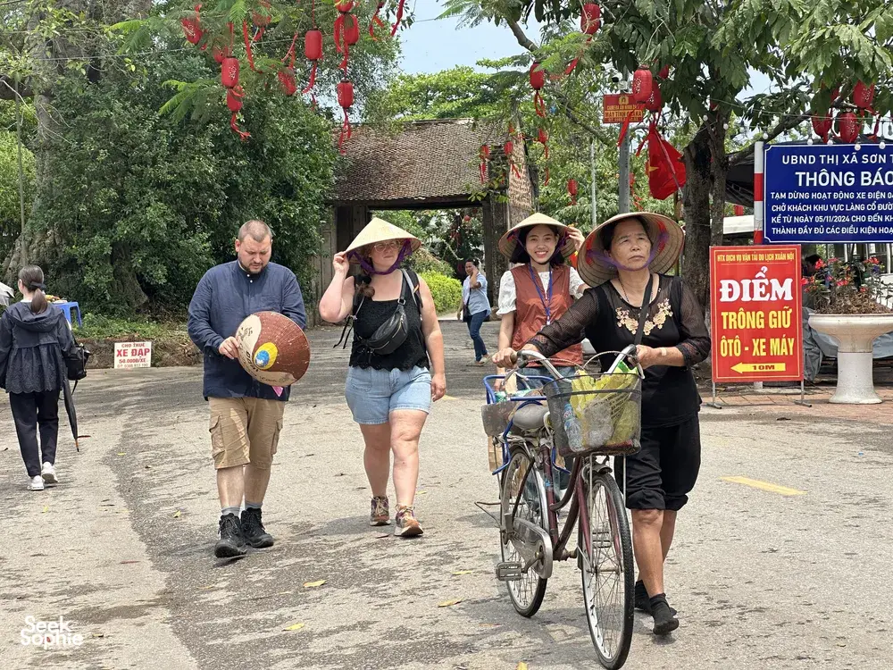 Travellers walking and cycling through Duong Lam ancient village near Hanoi, with red lanterns overhead and roadside signs