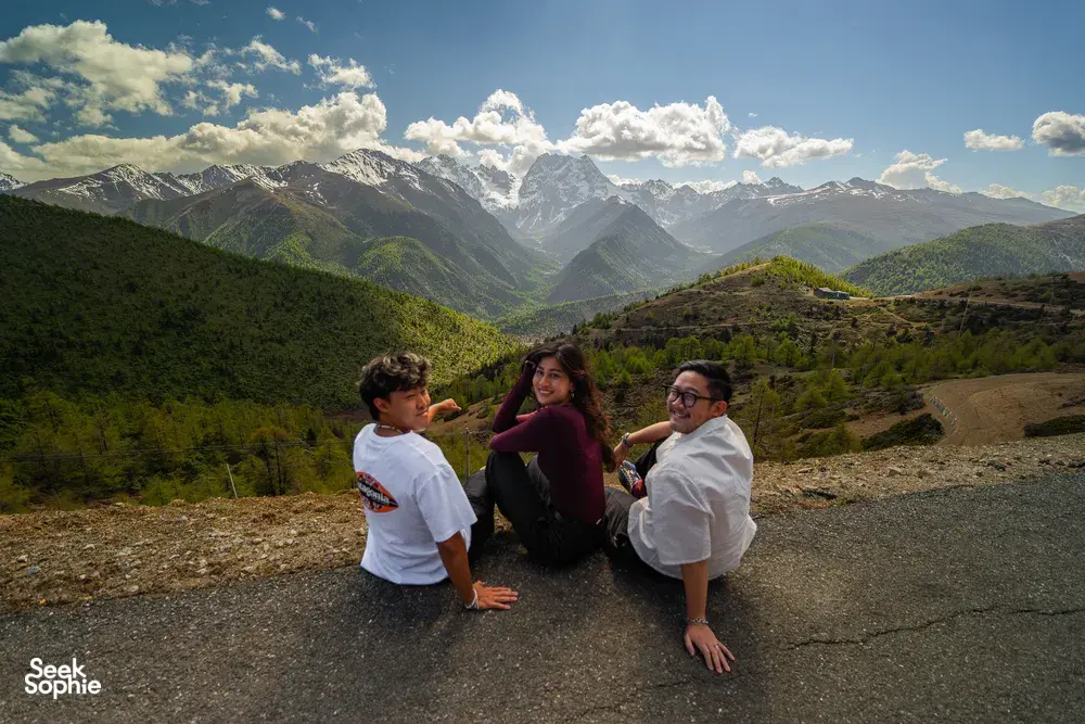 Travellers pausing on a gravel shoulder with sweeping valley hills and snow-dusted peaks during the 6-day Shangri-La Loop
