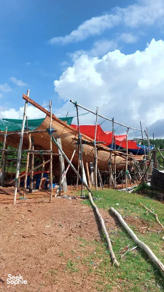 Rangka bot kayu dan jala nelayan di halaman berumput berhampiran hutan bakau yang subur di bawah awan yang dramatik, Labuan Bajo