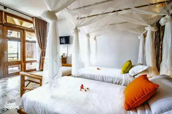 Luxurious double bed in a canopy-draped room at The Island Lodge in the Mekong Delta, with crisp white linens and bright cushions.