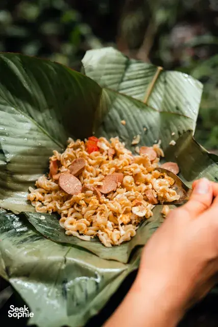 Hand placing orange elephant feed on banana leaves in Chiang Mai’s ethical sanctuary, part of the Hidden Doi Inthanon trails