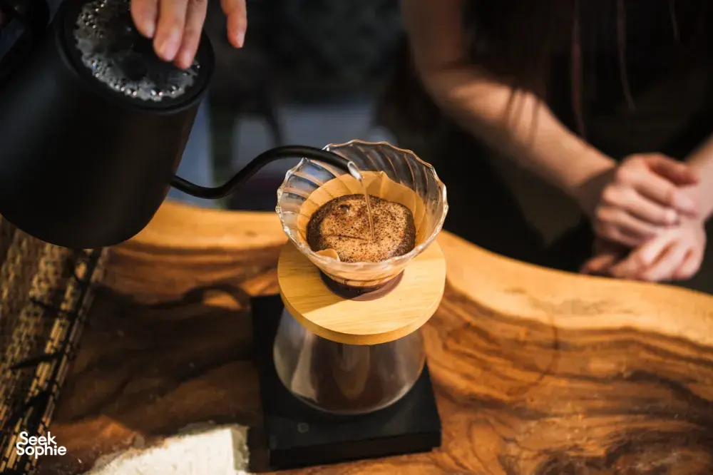 Pour-over coffee dripping into a glass dripper on a wooden table during hands-on coffee roasting workshops in Singapore