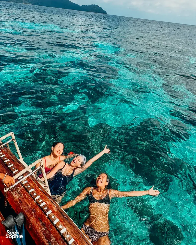 People swimming and snorkelling in clear turquoise water from a boat near Surin Island, with dark forested hills in view
