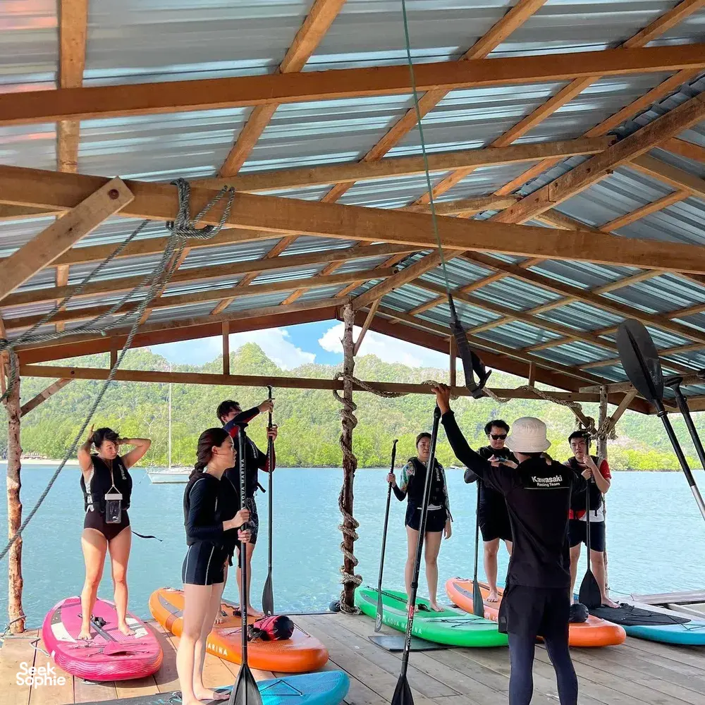 Host-led SUP briefing on colourful paddleboards under a seaside shelter at calm Tanjung Rhu, Langkawi