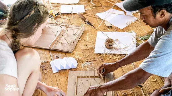Participants assembling a bamboo building prototype with cords and paper plans at a Bamboo Creative Bali design workshop in Bali
