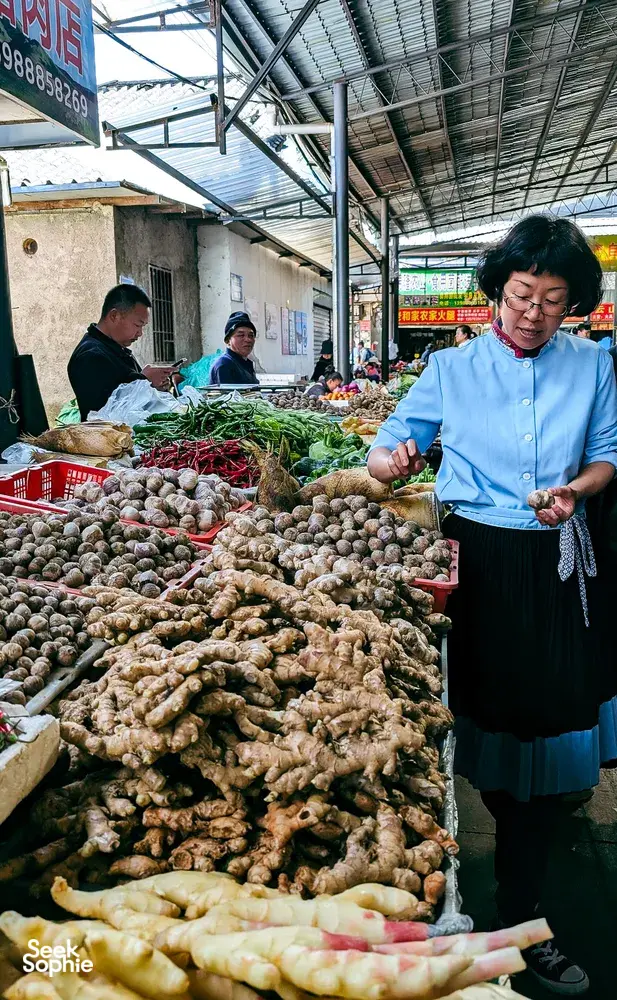 Fancy’s Yunnan host at a Lijiang market stall, selecting ginger and greens for the cooking class
