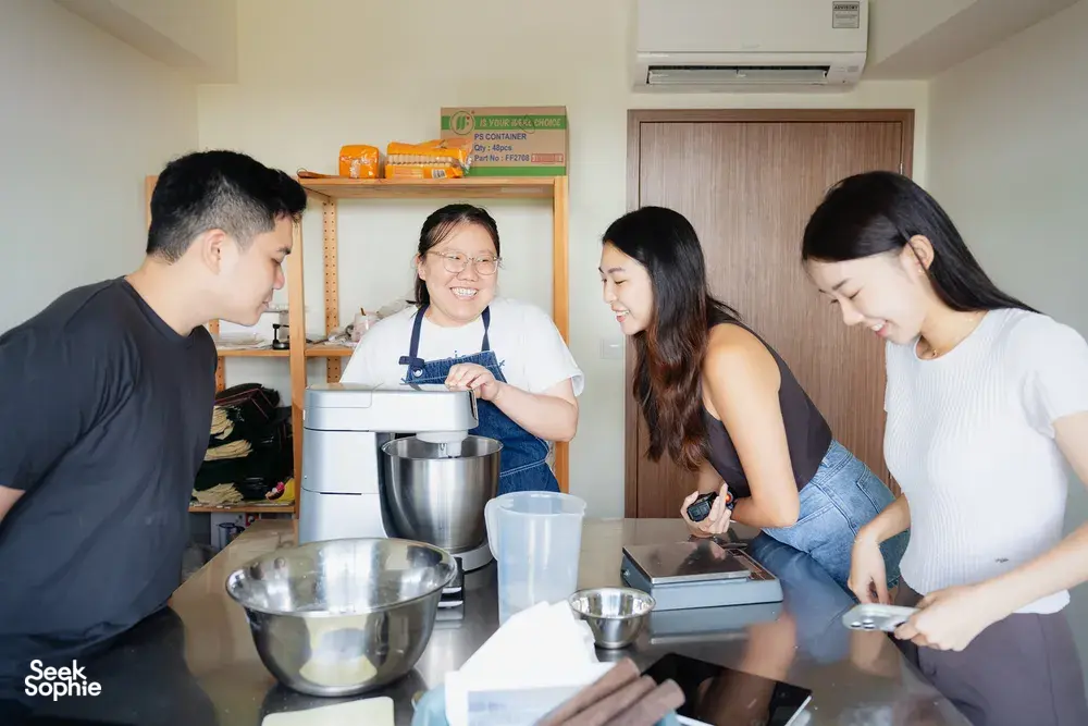 An instructor stirs dough at a stand mixer while learners shape pastries at benches, in hands-on baking workshops in Singapore