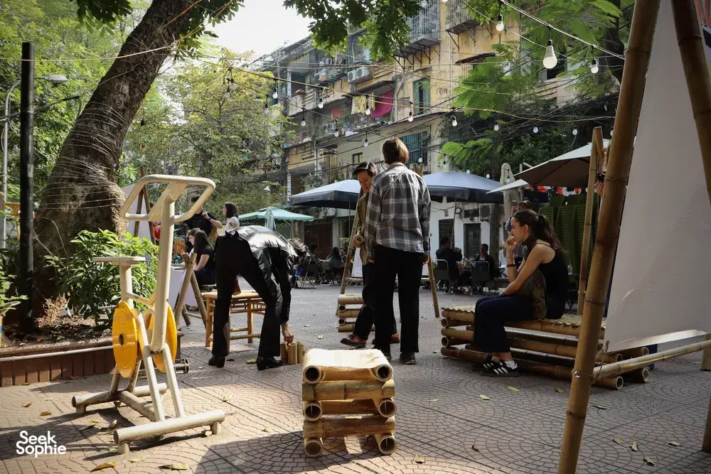 Community gathering in a shaded courtyard in Hanoi, with people relaxing near outdoor seats and swings under trees.