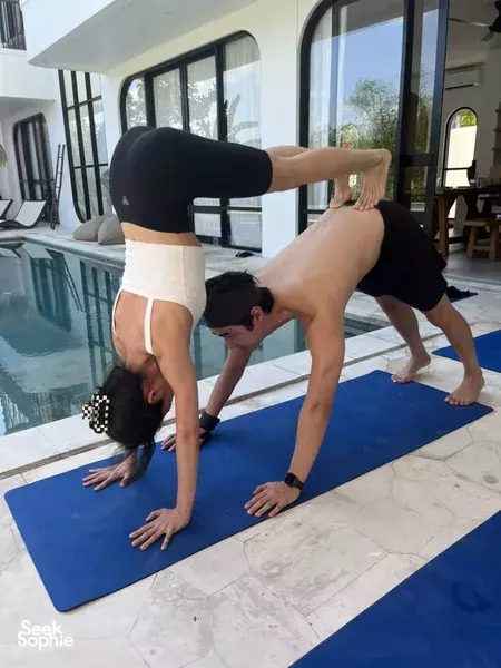 Two adults perform an inversion-style yoga pose on blue mats on a terrace beside the pool during a private Bali session, Canggu