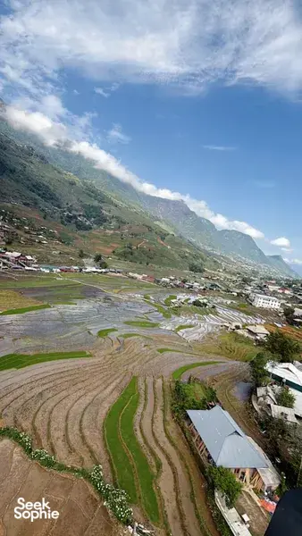 Patchwork rice terraces and small houses stretch across a mountain valley with cloud overhang, Sapa