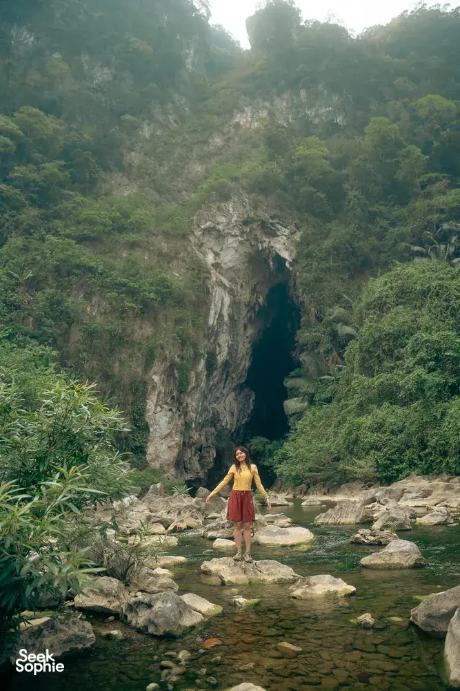 Woman standing in a shallow river with limestone cliffs and jungle in Phong Nha on a cave-and-fossils trip