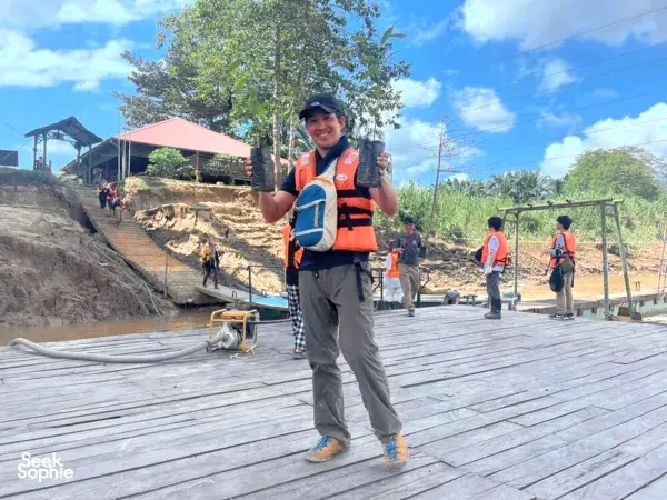 KOPEL Kinabatangan guide in an orange life vest smiles at a wooden jetty, ready for travellers on the Kinabatangan River