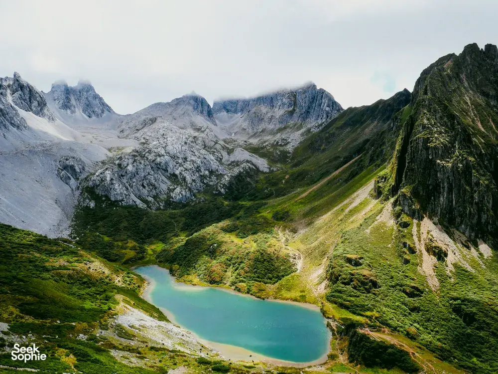 Hidden alpine lake in Shangri-La with turquoise water, mountain paths and glaciers beyond on a trek panorama