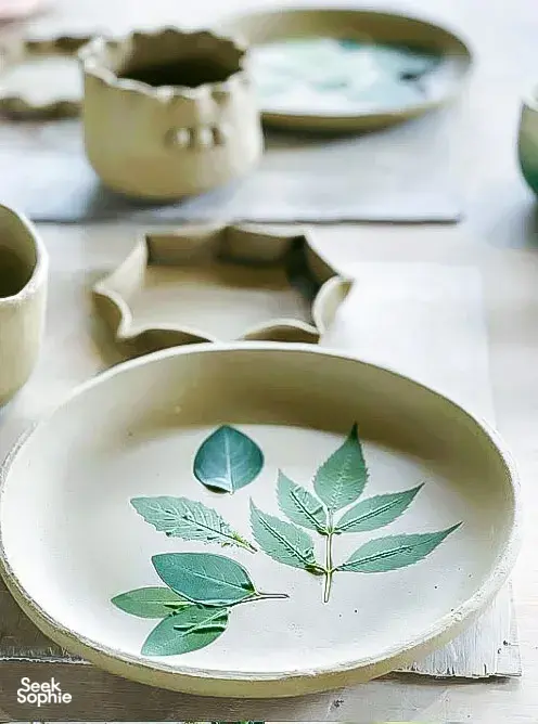 Green-leaf painted ceramic plate on a worktable in Ilham Ceramic Studio, Langkawi, with other bowls blurred behind