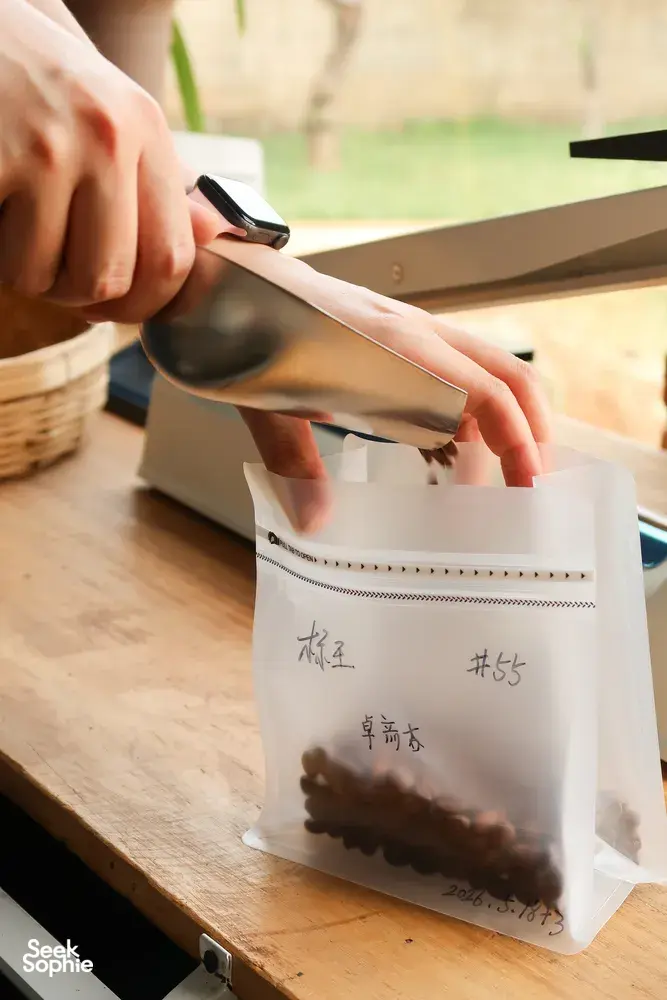 Hands sealing labelled coffee sample bags on a wooden table during packing at Seeker Yunnan Coffee Estate in Lijiang