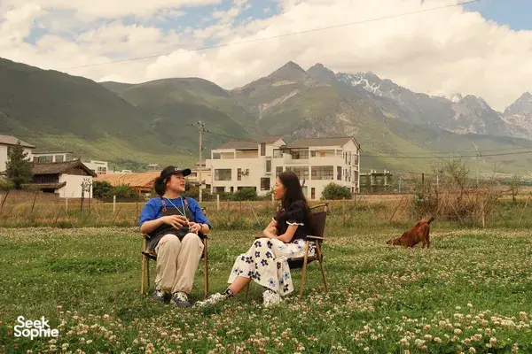 Outdoor coffee tasting with Seeker Yunnan Coffee Estate host and guest in Lijiang, surrounded by wildflowers and mountains