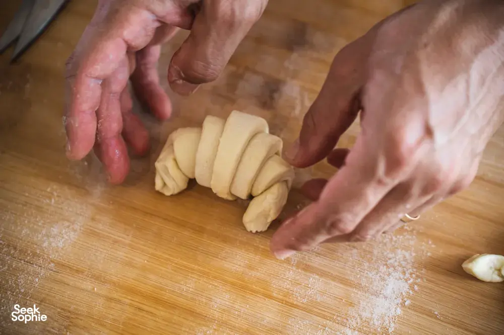 Hands portioning and rolling croissant dough on a floured wooden worktop in a home kitchen in Singapore — workshops in Singapore