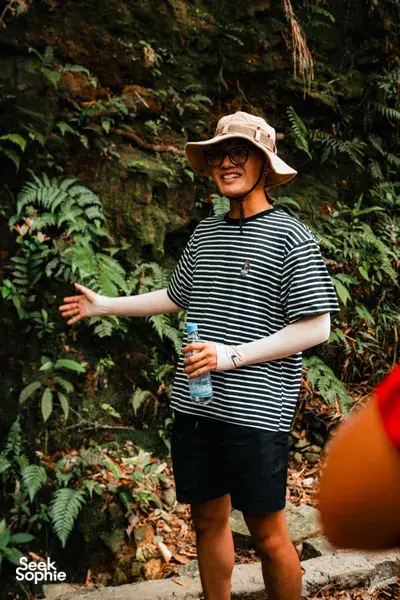 Smiling traveller in a hat on a forest trail in Bach Ma near Da Nang, surrounded by ferns during the 2D1N camping