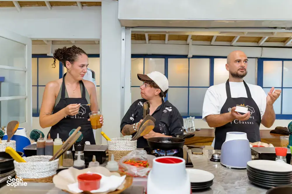 Gili Islands cooking class in Lombok: participants sip drinks and cook at cooking stations, sharing peanut-sauce flavours